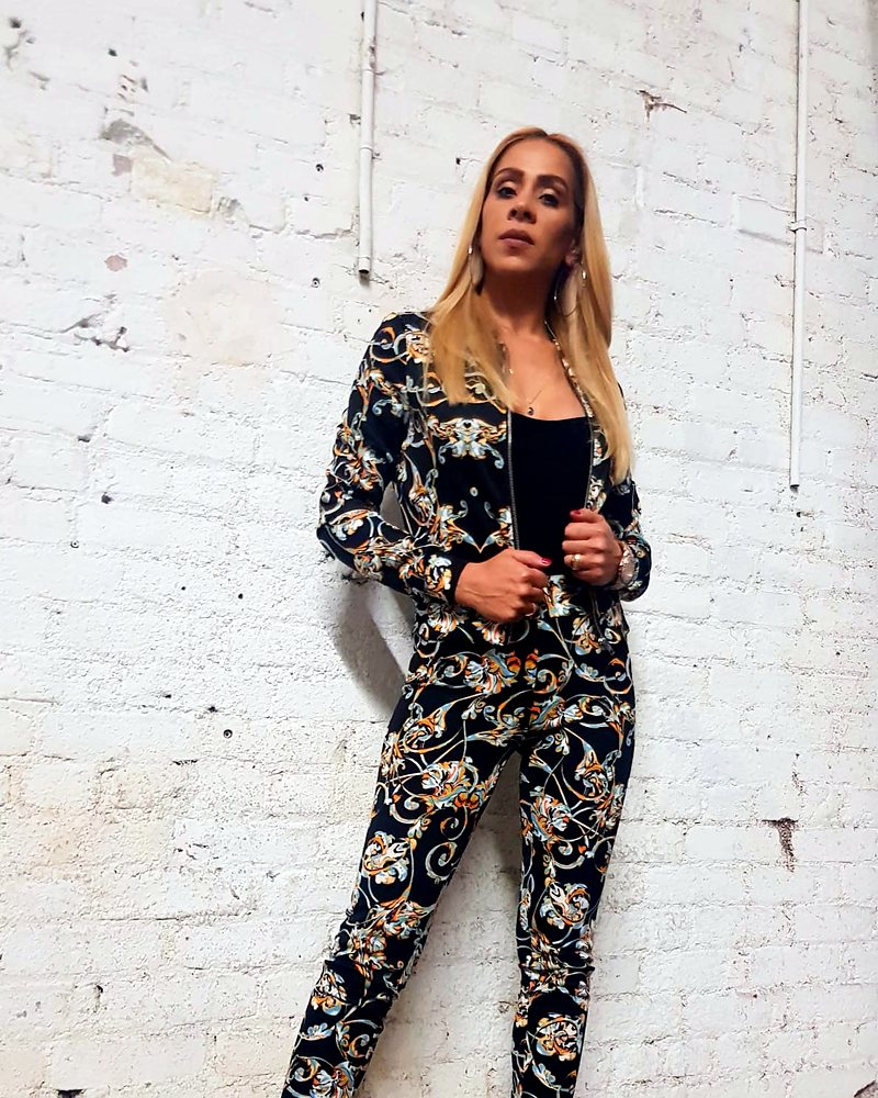 Inbar in a floral suit against a white brick wall