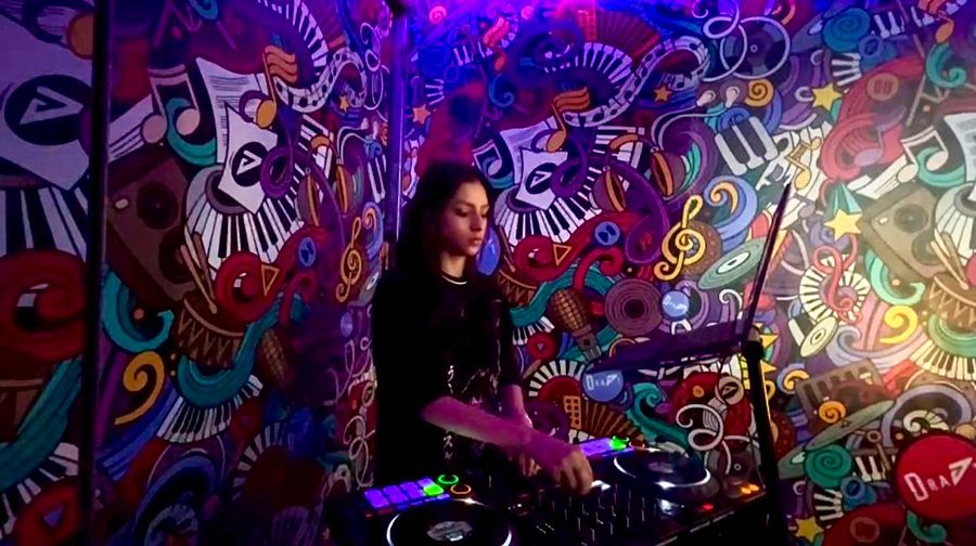 DJ Jaqueline at the decks in front of a colourful mural
